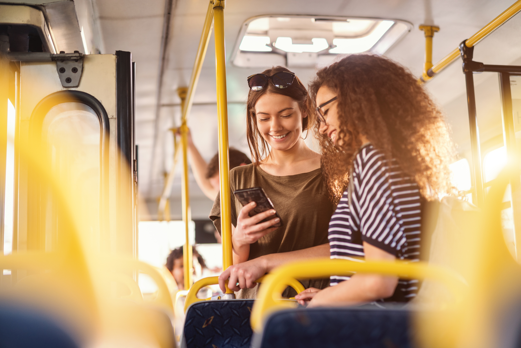 Two young women on public transport looking at a mobile together smiling