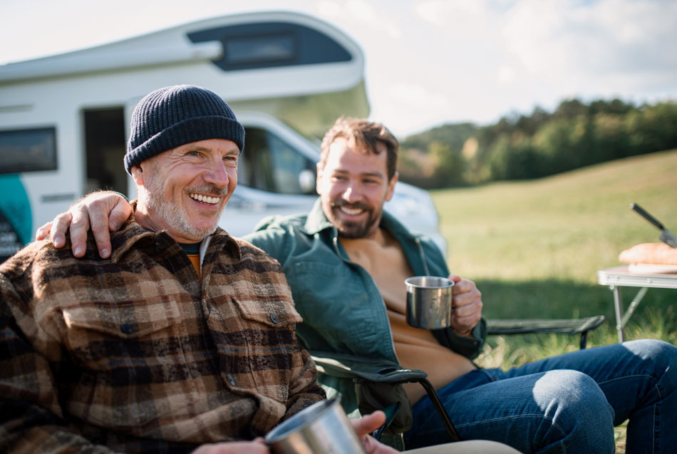 Two men sitting in front of a camper van enjoying a drink